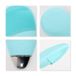 A silicone facial cleansing brush in light blue, featuring textured surfaces and a sleek metallic base.