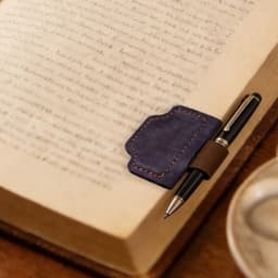 A navy blue magnetic bookmark with a pen clip resting on an open book, with a pen attached for convenience.
