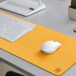 A bright yellow PU leather desk mat with a white mouse and a keyboard on a grey desk. It features a logo in one corner.