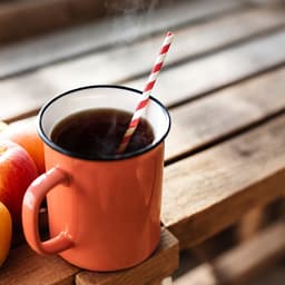 A drink bottle with a red and white striped disposable paper straw, placed on a wooden surface beside fresh apples.