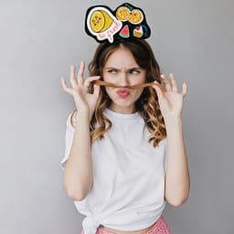 A woman playfully poses with a custom felt headband featuring fruit designs and a logo, set against a plain background.