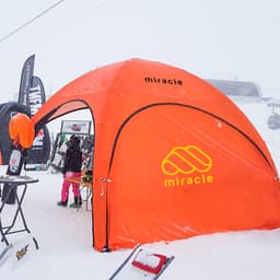 An orange inflatable marquee with a logo, set in a snowy outdoor environment, showcasing an exhibition space.
