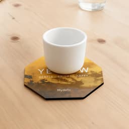 An octagonal frosted metal coaster in yellow and black, featuring a white cup placed on top.