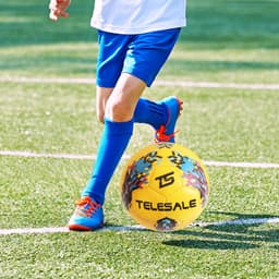 A training soccer ball in yellow with a colourful design, placed on green grass, as a child runs by.