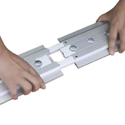 Two hands connecting segments of a silver LED light box display with visible connectors and mounting points.