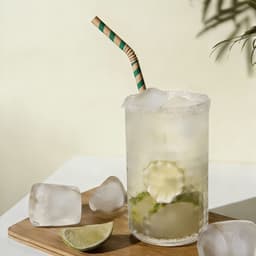 A glass of cocktail with ice, garnished with lime slices, features a green and white striped bendable paper straw.