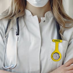 A yellow silicone nurse watch attached to a white lab coat, alongside a stethoscope.