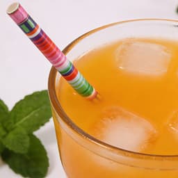 A drink bottle filled with orange liquid and ice, featuring a colourful striped 4-ply paper straw and mint leaves.