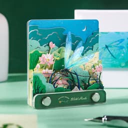 A 3D paper-cut sculpture notepad featuring a vibrant nature scene with dragonflies, flowers, and greenery, in various shades of blue and green.