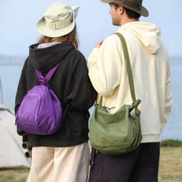 A purple lightweight convertible backpack and a green duffel bag, held by two people wearing casual outfits and hats.