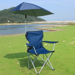 A navy blue adjustable umbrella attached to a folding camping chair by a universal clamp, set by a lake.