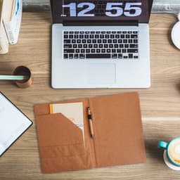 A4 cork folder in natural brown, open to reveal a notepad and pen, placed on a wooden desk with a laptop.