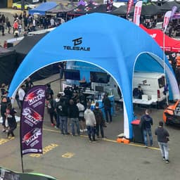A blue inflatable marquee with a logo, set up in a busy event area, surrounded by people and banners.