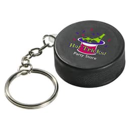 A black hockey puck stress reliever attached to a metal keyring, featuring a logo on the surface.