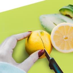 A bright green foldable chopping board with a hand cutting a lemon on it, featuring a sliced lemon beside it.