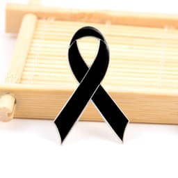 A black metal lapel pin shaped like a ribbon, resting on a bamboo surface.
