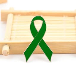 A green metal lapel pin shaped like a ribbon, displayed on a bamboo tray.