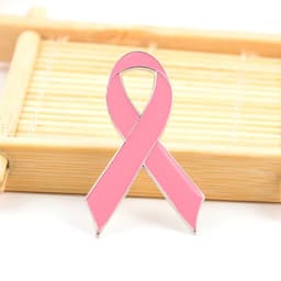 A pink ribbon metal lapel pin with a shiny silver outline, set against a wooden background.
