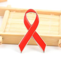 A red metal lapel pin shaped like a ribbon, displayed on a bamboo tray. It features a shiny finish and has a logo.