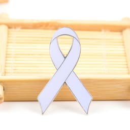 A white metal lapel pin shaped like a ribbon, displayed on a bamboo mat. It features a logo.