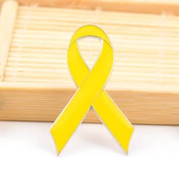 A yellow ribbon metal lapel pin with a shiny finish, displayed on a wooden surface.