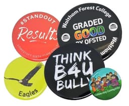 A collection of five button badges in various colours featuring different designs and logos.