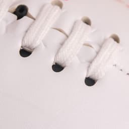 A close-up of a white mini footy ball showing laces and stitching details. There is a logo on the surface.