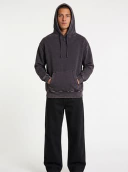 A men's stone wash fleece hoodie in dark grey, featuring a front pocket and a hood, styled with black trousers.
