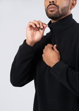 A black polar fleece half zip top with a high collar and a zipper, featuring a person adjusting the zip.