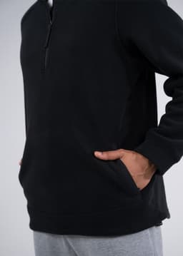 A black polar fleece half zip top with side pockets, featured on a model wearing grey pants.