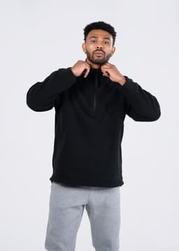 A man wearing a black polar fleece half zip top paired with grey trousers, standing against a plain background.