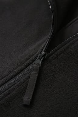 A close-up of a black polar fleece half zip top, featuring a smooth zipper detailing.