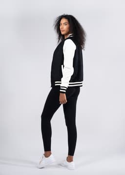 A black and white women's varsity jacket with a soft shell wool blend, modelled alongside black leggings and white shoes.
