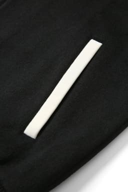 A close-up of a black wool blend soft shell varsity jacket featuring a white pocket detail and a logo.