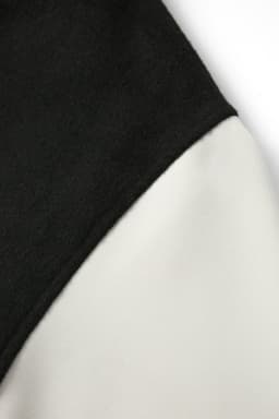 A close-up of a men's/unisex wool blend varsity jacket with black and cream fabric. It features a branding logo.