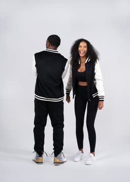 A black and cream varsity jacket worn by a woman and a man, featuring a logo on the back.