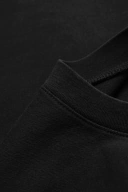 A close-up of a black oversized T-shirt made from 230gsm 100% organic cotton, featuring a simple neckline and fabric texture.