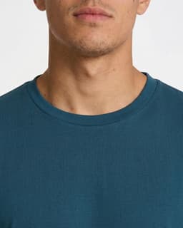 A close-up of a men's/unisex t-shirt in a dark teal colour, featuring a round neckline and no visible branding.