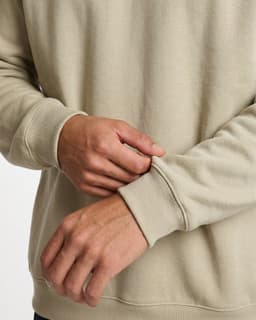 A beige poly cotton fleece jumper featuring fitted cuffs and a relaxed fit. The image highlights a person's hands adjusting the sleeve.