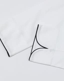 A white unisex executive chef jacket with black piping details on the cuffs. It features a clean, professional design.