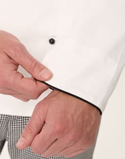 A close-up of a white executive chef jacket featuring black piping, highlighting the cuff detail and button.