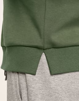 A green crew neck sweater featuring ribbed hem details and a split at the bottom, paired with grey joggers.