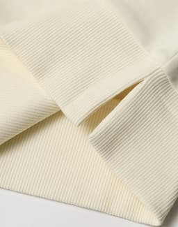 A close-up of a cream-coloured unisex crew neck sweater, featuring ribbed cuffs and hem. It has a logo.