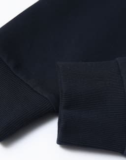 A close-up of a navy unisex crew neck sweater featuring ribbed cuffs and a smooth finish. Contains a logo.