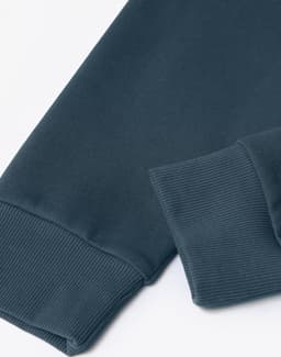 A close-up of a dark teal unisex crew neck sweater, featuring ribbed cuffs and a smooth texture.