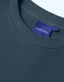 A close-up of a navy unisex crew neck sweater featuring a ribbed neckline and a small logo tag.