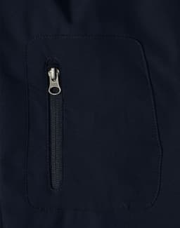 A close-up of a navy softshell jacket featuring a zippered pocket. The fabric appears smooth and durable.