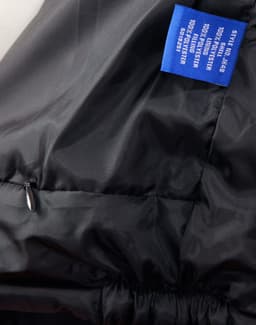 A black heavy quilted jacket featuring a zippered pocket and a label with branding.