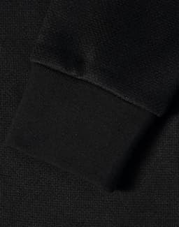 A close-up of a black jacquard fleece jacket's textured fabric and cuff. Features a logo.