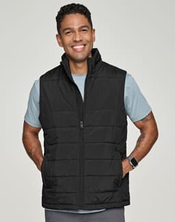 A man wearing a black insulated puffer vest with a 3D cut over a grey shirt, smiling. The vest has a logo.